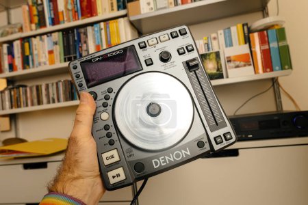 Foto de París, Francia - 30 de octubre de 2023: Una mano masculina presenta una plataforma DJ Denon Professional DN-S1000, con una colección de estantes de audio en el fondo de una sala de estar bien equipada - Imagen libre de derechos