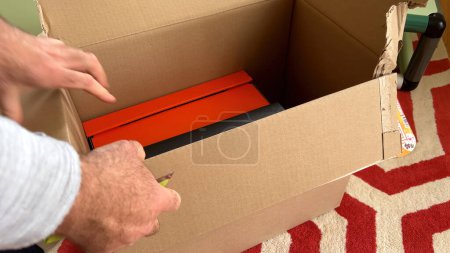Téléchargez les photos : Paris, France - Sep 2023 : Une main masculine ouvre méticuleusement un carton orange et noir plus petit de l'intérieur d'une boîte en carton plus grande, dévoilant le contenu avec anticipation. - en image libre de droit
