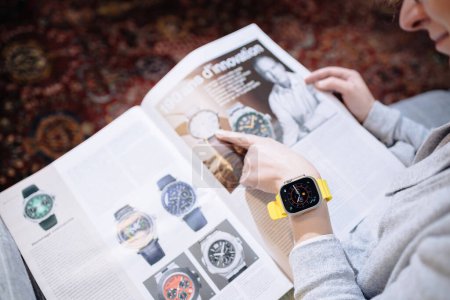 Foto de Londres, Reino Unido - 28 de septiembre de 2022: Una mujer elegante se adorna la muñeca con el nuevo Apple Watch Ultra 2 mientras está absorta en una revista de moda con relojes suizos e internacionales, que muestra - Imagen libre de derechos