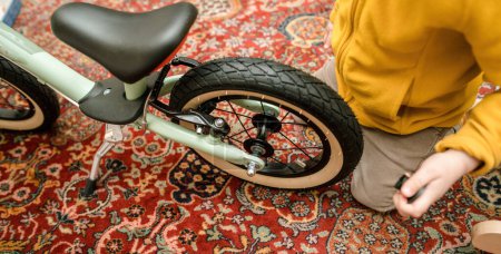 Photo for An impatient toddler eagerly gazes at his new learning bike in the living room during the unboxing and assembly process, filled with excitement for his new ride - Royalty Free Image