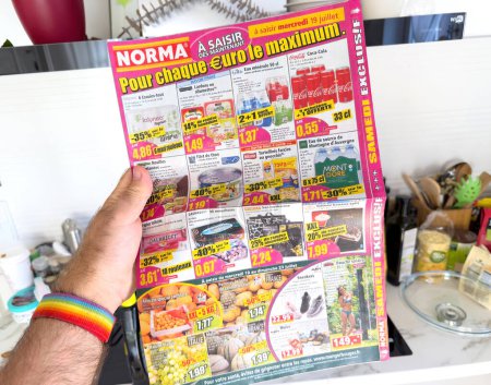 Foto de Mano masculina se ve sosteniendo y leyendo cuidadosamente un papel publicitario de Norma Supermarket en Francia con precios con descuento en varios artículos. - Imagen libre de derechos