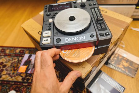 Foto de París, Francia - 24 de octubre de 2023: Se ve una mano masculina insertando un CD en el nuevo controlador Denon Professional DN-S1000 DJ, preparándose para probar y mezclar - Imagen libre de derechos