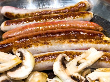 Téléchargez les photos : Délicieuses saucisses chaudes associées à la cuisson des champignons dans une casserole, incarnant le concept d'un déjeuner parfait avec une température chaude - en image libre de droit