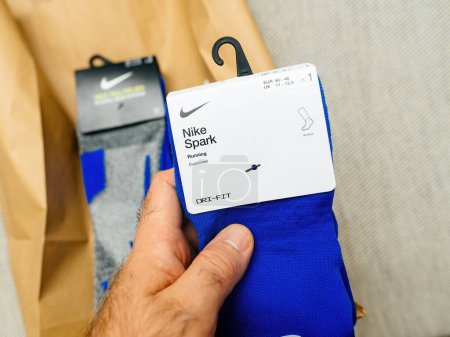 Téléchargez les photos : Paris, France - 25 octobre 2023 : Vue à la première personne d'un homme tenant une nouvelle paire de chaussettes de course Nike Spark bleues équipées de la technologie Dri-FIT - en image libre de droit