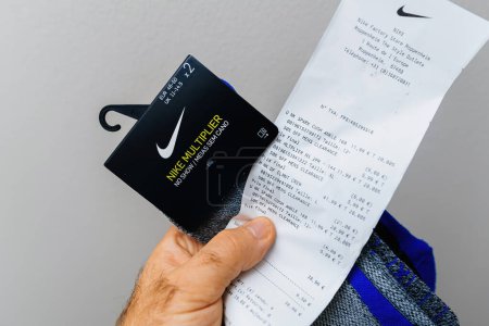 Foto de París, Francia - 30 de octubre de 2023: una mano masculina que sostiene los calcetines Nike Multiplier sin presentación junto con un recibo del Roppenheim Fashion Outlet. - Imagen libre de derechos