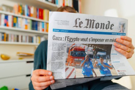 Téléchargez les photos : Paris, France - 3 oct. 2023 : Une femme immergée dans la dernière presse française, Le Monde, avec un titre discutant de la volonté égyptienne de servir de médiateur entre le Hamas et Israël, fournissant les dernières nouvelles sur la - en image libre de droit