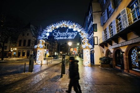 Téléchargez les photos : Une silhouette masculine méconnaissable se promène dans une rue vide avec en arrière-plan le panneau de Strasbourg Capitale de Noel, créant un contraste saisissant - en image libre de droit