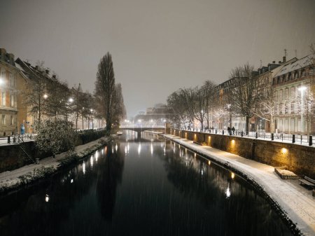 Téléchargez les photos : Photographie nocturne de Strasbourg recouverte de neige lors d'une tempête de neige, avec la rivière Ill, plusieurs étangs et des bâtiments de style haussmannien - en image libre de droit