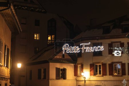 Foto de Petite France señales de calle brillan en medio de las luces de Navidad, contra un telón de fondo de apartamentos, anunciando Strasbourgs temporada festiva - Imagen libre de derechos