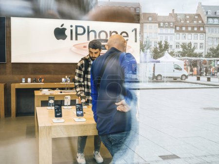 Foto de París, Francia - 22-sep-2023: Una vista a través del vidrio escaparate revela a los clientes que exploran el último iPhone 15 Pro en una tienda Apple en su día de lanzamiento - Imagen libre de derechos