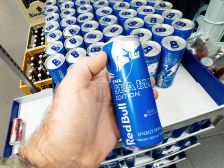 Photo for Frankfurt, Germany - Nov 10, 2023: A male hand holds a metallic can of Red Bull Sea Blue Edition energy drink, purchased for its refreshing qualities from a store - Royalty Free Image