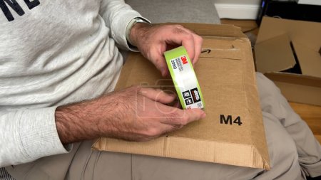 Photo for Paris, France - Sep 22, 2023: A close-up view captures a male hand skillfully unboxing a 3M Scotch tape from an Amazon Prime M4 size cardboard parcel - Royalty Free Image