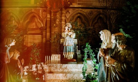 Téléchargez les photos : Une crèche vibrante à l'intérieur de Notre-Dame de Strasbourg, avec des personnages en prière solennelle au milieu de verdure festive et de chandeliers - en image libre de droit