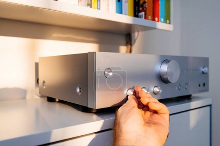 Photo for Frankfurt, Germany - Dec 12, 2022: A mans hand is shown adjusting the bass on a new Onkyo professional power amplifier on Vitsoe 606 shelves, in a modern high-tech interior - Royalty Free Image