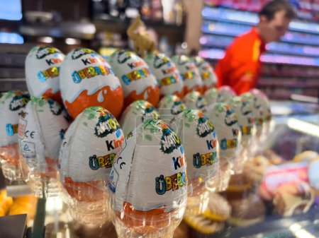 Foto de Frankfurt, Alemania - 20 de diciembre de 2022: Filas de Kinder Sorprende los huevos de chocolate en una tienda, con una figura borrosa en el fondo, evocan un sentido de deleite infantil - Imagen libre de derechos