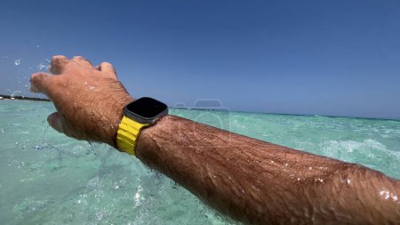 Téléchargez les photos : Bras atteignant à travers l'eau de mer claire, portant une montre intelligente, capturant l'essence de la technologie moderne dans les loisirs aquatiques - en image libre de droit