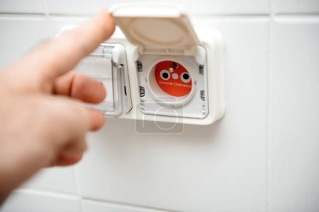 Photo for Male hand opening a power socket with a red tag, featuring French text translated as computer safety outlet emphasizing security - Royalty Free Image