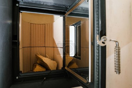 Foto de Primer plano de una estufa de azulejos planos de nueva instalación con una puerta abierta, que revela el interior prístino de la cámara de combustión - Imagen libre de derechos