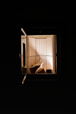 Foto de Troncos de madera dentro de una nueva estufa de baldosas planas con una puerta abierta, mostrando un interior limpio y luz cálida de una lámpara interna - Imagen libre de derechos
