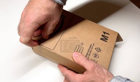 Foto de París, Francia - 23 de febrero de 2023: Un hombre abre una caja de cartón Amazon Prime, capturando el momento de presentar una nueva compra al minorista en línea - Imagen libre de derechos