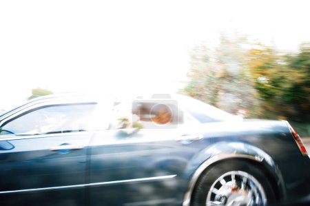 Téléchargez les photos : Une silhouette déconcentrée d'une personne à l'intérieur d'une voiture de luxe, capturée en mouvement, tenant un bouquet de fleurs, soulignant le cadre dynamique et élégant - en image libre de droit