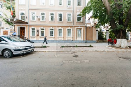 Téléchargez les photos : Chisinau, Moldavie - 30 sept. 2011 : Façade de la Cour constitutionnelle de Moldavie avec une voiture Renault garée, un piéton et un employé détendu à l'entrée de l'escalier - en image libre de droit