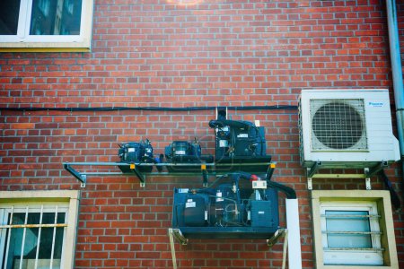 Téléchargez les photos : Thionville, France - 10 juin 2016 : Compresseurs hermétiques multiples près d'une thermopompe à air conditionné Daikin sur la façade d'une maison en brique, vue à faible angle - en image libre de droit