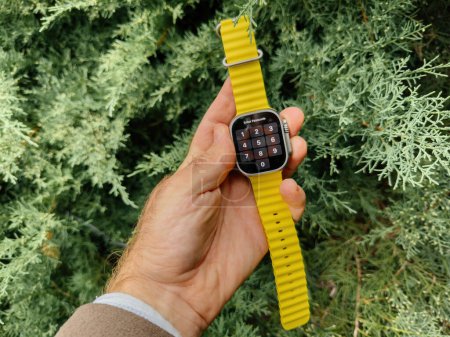 Foto de Londres, Reino Unido - 23-sep-2022: Experimenta el modo nocturno en el nuevo Apple Watch Ultra 2 de titanio para una mejor visualización en condiciones de poca luz, con un sereno arbusto de enebro en el fondo - Imagen libre de derechos