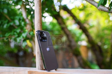Foto de Londres, Reino Unido - 28 de septiembre de 2022: El último teléfono inteligente Apple iPhone 14 Pro en un lujoso color violeta, que se muestra elegantemente en una valla de madera con un fondo bokeh verde vibrante - Imagen libre de derechos