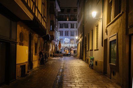 Photo for Strasbourg, France - Dec 18, 2022: A male silhouette walks Strasbourgs illuminated city streets, smoking and surfing his phone during the annual Christmas market. Pizzeria sign in background - Royalty Free Image
