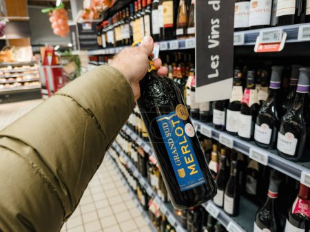 Téléchargez les photos : Paris, France - 10 nov. 2023 : Point de vue d'un homme tenant une bouteille de vin rouge Grand Sud Merlot d'un litre lors d'achats de vacances dans un supermarché français - en image libre de droit