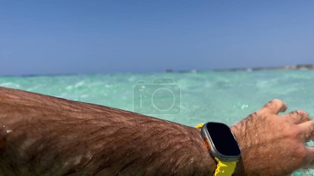 Téléchargez les photos : Majorque, Espagne - 6 juin 2023 : Une main masculine plonge dans les eaux colorées et propres de Majorque avec une nouvelle Apple Watch Ultra 2, sur fond de ciel bleu serein - en image libre de droit