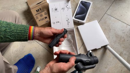 Foto de París, Francia - 10 de junio de 2023: Una mano masculina examina varios accesorios para el nuevo estabilizador de teléfonos inteligentes DJI Osmo Mobile 6, recientemente entregado a través de Amazon Prime - Imagen libre de derechos