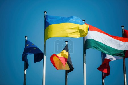 Téléchargez les photos : The Ukrainian flag waves proudly next to the European Union flag and other EU country flags, set against a clear, peaceful blue sky - en image libre de droit