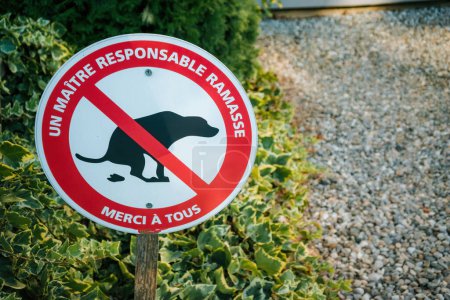 French sign prohibiting dog fouling, urging owners to be responsible, against a backdrop of green foliage and gravel.