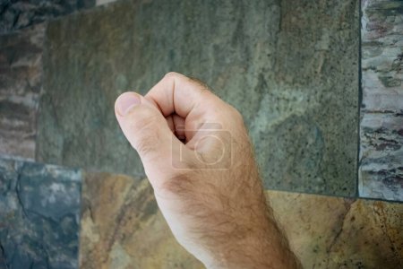 Photo for A male fist clenched in determination or solidarity, set against a multi-textured stone wall, embodying strength and resilience. - Royalty Free Image