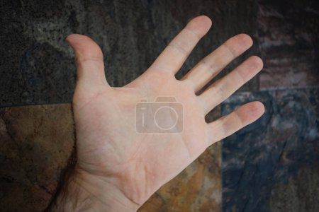 Photo for Close-up of a males open hand extended forward, with detailed skin texture against a dark stone background. - Royalty Free Image