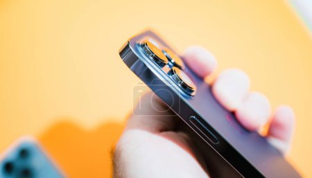 Téléchargez les photos : Paris, France - Sep 29, 2022: Male hand presenting the new Apple iPhone 14 Pro with a yellow background, utilizing a tilt-shift lens to highlight this latest computing device. - en image libre de droit