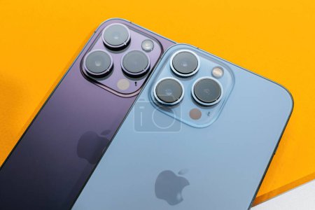 Photo for Paris, France - Sep 29, 2022: Two high-end Apple iPhone models, 13 Pro and 14 Pro, showcased together against a yellow background with distinct logotypes and pro camera modules - Royalty Free Image