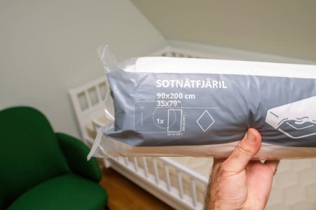 Photo for Paris, France - Oct 27, 2022: POV of a male hand holding the SOTNATFJARIL Waterproof Mattress Protector package, 90x200 cm, on a new mattress in a childs room - Royalty Free Image