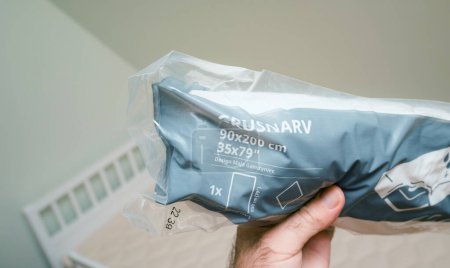 Téléchargez les photos : Paris, France - Oct 27, 2022: Male hand holding a new package of IKEA GRUSNARV Waterproof Mattress Protector, size 90 x 200 cm, in a baby room with a newly installed bed - en image libre de droit