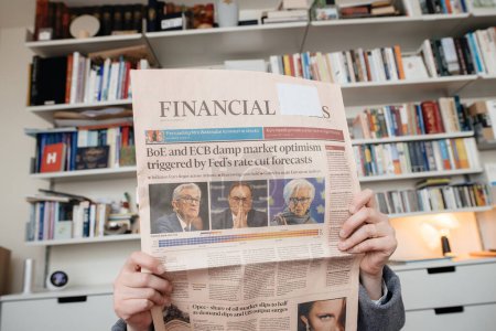 Foto de Paris, France - Dec 20, 2023: A woman in a living room reads the latest Financial Times, featuring headlines about the BoE and ECBs impact on market optimism after the Feds rate cut - Imagen libre de derechos