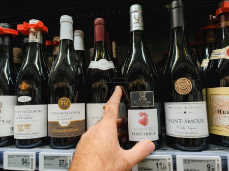 Foto de PAris, Francia - 10-nov-2023: Una mano masculina eligiendo una botella de Saint Amour, a un precio de 11.07 euros, un vino tinto codiciado, perfecto para los entusiastas del vino más exigentes. - Imagen libre de derechos