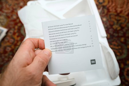Photo for Paris, France - Nov 16, 2023: A male hand holding the multilingual user manual of the newly unboxed Mi Smart LED Desk Lamp Pro, highlighting its features - Royalty Free Image