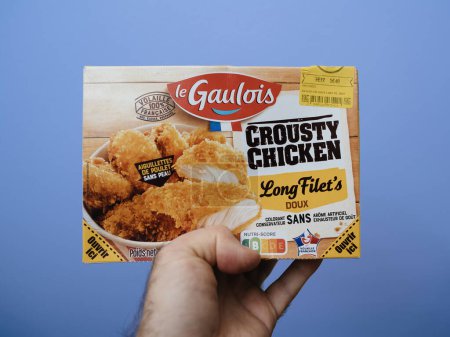 Foto de París, Francia - 20 de diciembre de 2023: Una mano de hombre presenta un paquete de pollo Le Gaulois Crousty, listo para la preparación rápida del horno. - Imagen libre de derechos