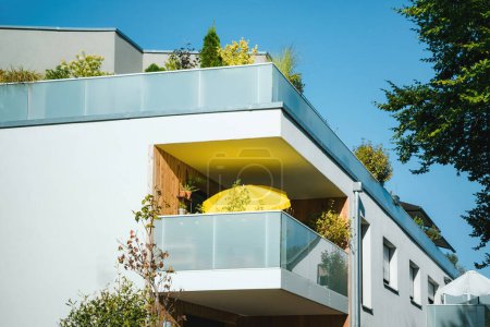 Photo for Contemporary apartment balcony adorned with green plants and furnished with a round yellow table, highlighting urban outdoor living on a clear sunny day - Royalty Free Image