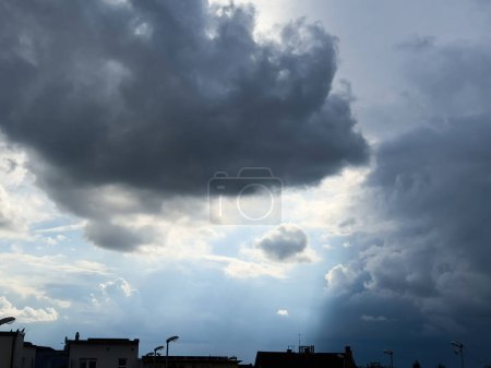 Photo for Imposing dark clouds loom above an urban skyline, with rays of light piercing through, signaling an approaching storm - Royalty Free Image