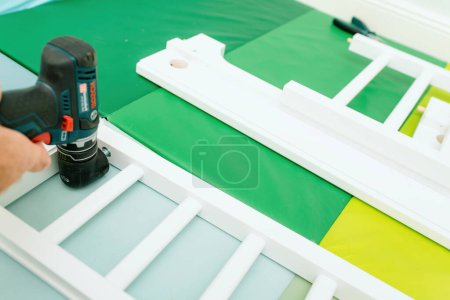 Photo for Paris, France - Oct 27, 2022: A craftsmans hand operates a Bosch power tool for assembling white furniture pieces on a vibrant green mat - Royalty Free Image
