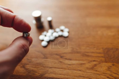 Photo for A person carefully picks up a small button battery from a wooden surface, highlighting meticulous effort in a detailed task. - Royalty Free Image