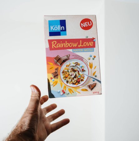 Photo for Frankfurt, Germany - Jun 12, 2023: A hand is presented against a white background, playfully appearing to catch a falling box of Kolln Rainbow Love muesli cereal, as though capturing a vibrant - Royalty Free Image